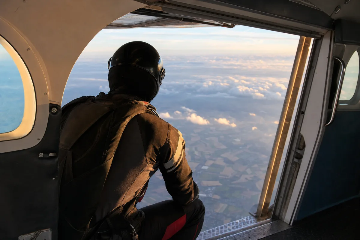 Primo-sautant harnaché regardant par la porte ouverte de l’avion en altitude