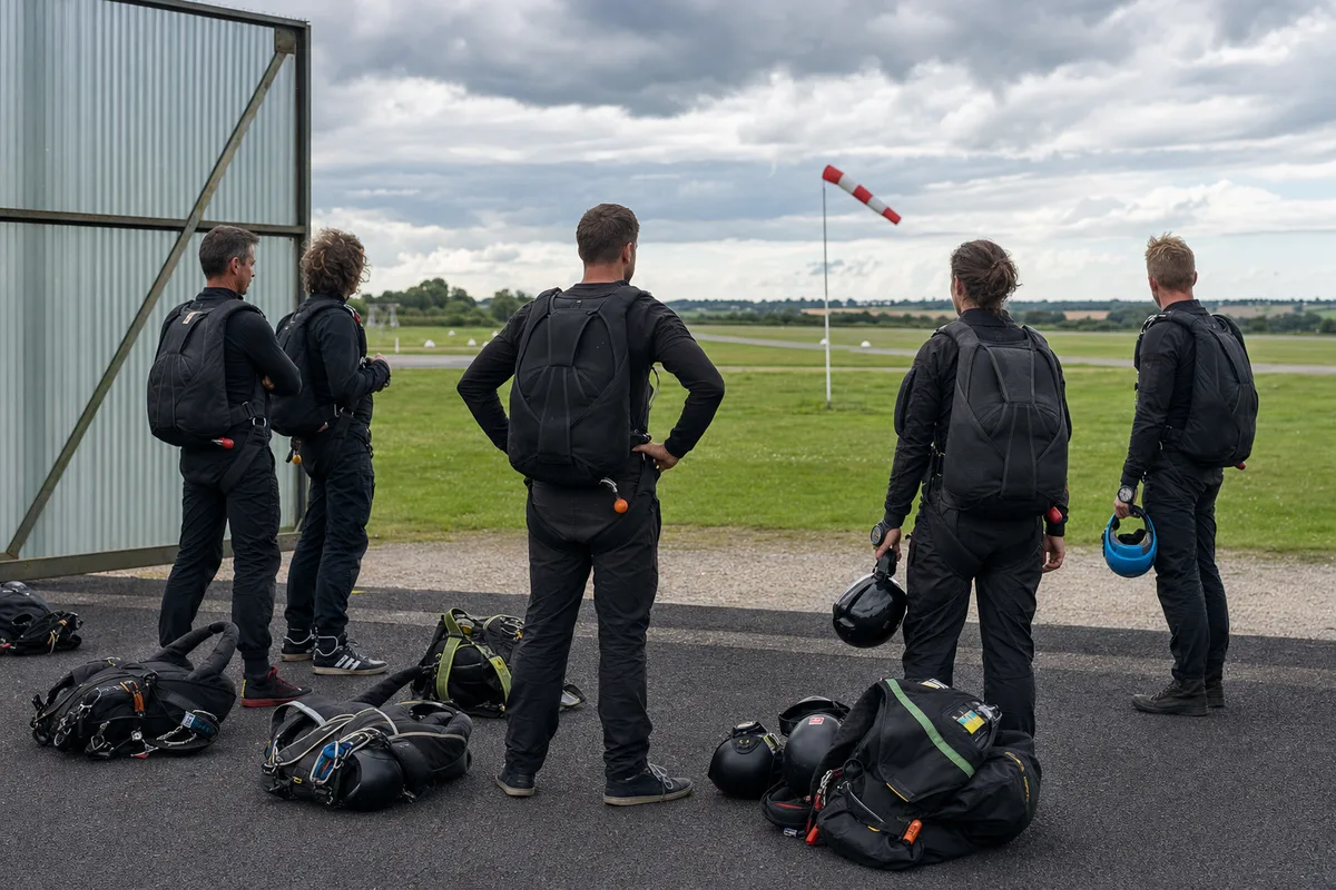 Élèves parachutistes en briefing au sol devant un hangar d’aérodrome normand